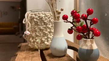 Vasen mit Beeren und Zweigen auf Holztisch.