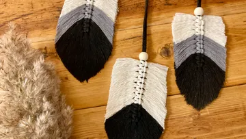 Macramé arrows on wooden table, pampas grass nearby.