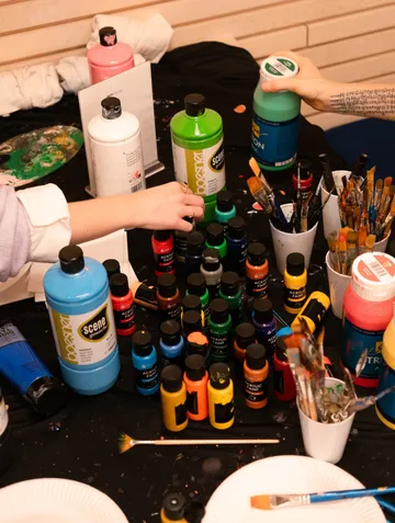 Hands reaching for paint bottles on table.