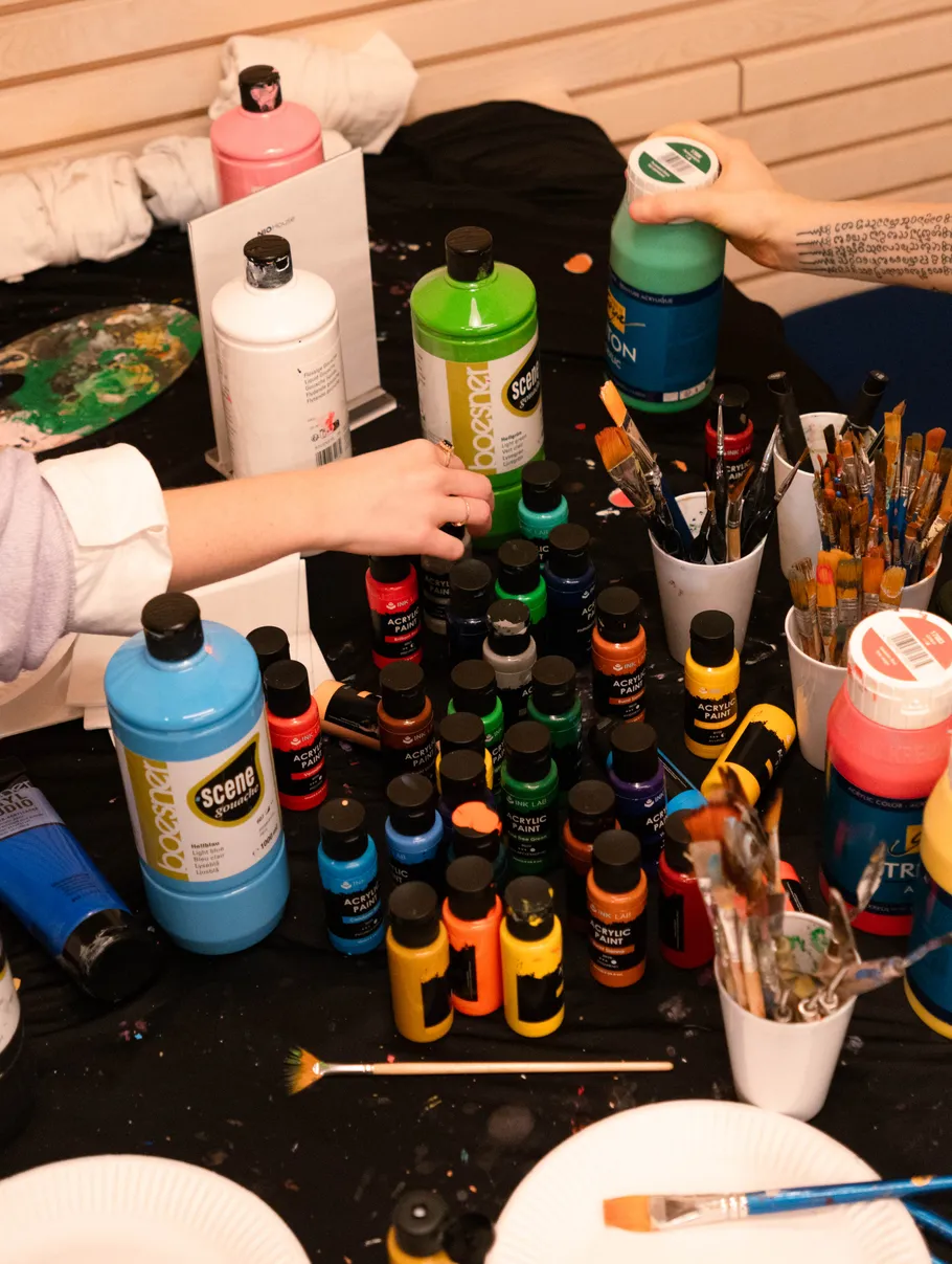 Hands reaching for paint bottles on table.
