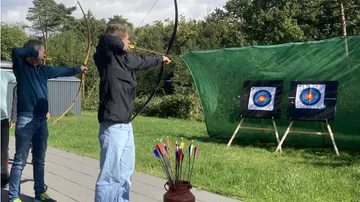 Men aiming bows at archery targets outdoors.