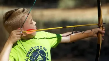 Boy aiming bow and arrow outdoors.