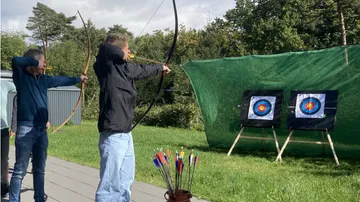Two people practicing archery outdoors at targets.