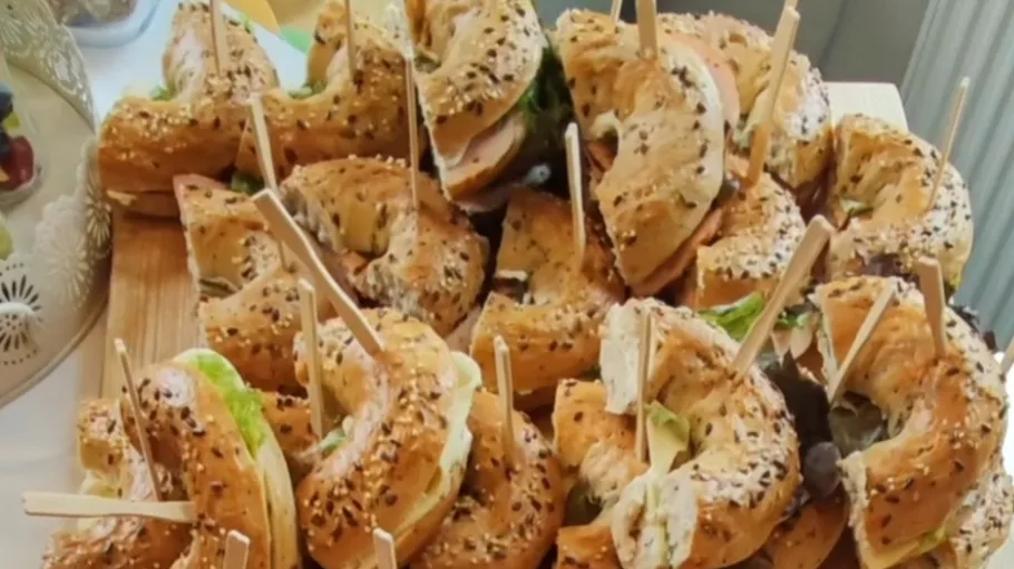 Bagel sandwiches stacked with wooden skewers on tray.