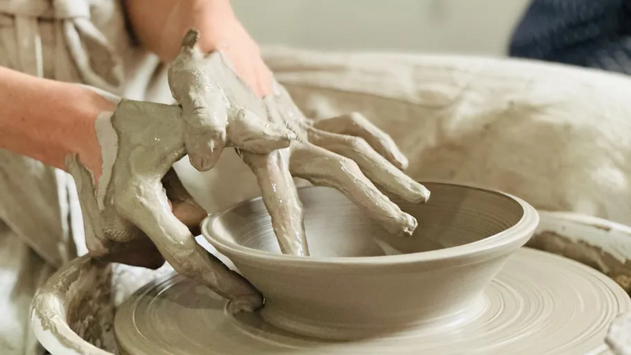 Hands shaping clay on spinning pottery wheel.