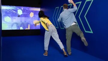 Zwei Personen werfen Bälle auf einen Bildschirm.