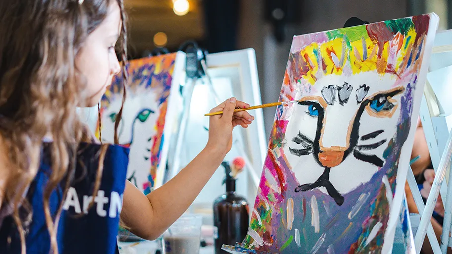 Child painting colorful lion on canvas indoors.