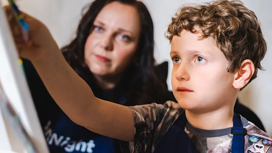 Child painting on canvas, adult supervising closely.