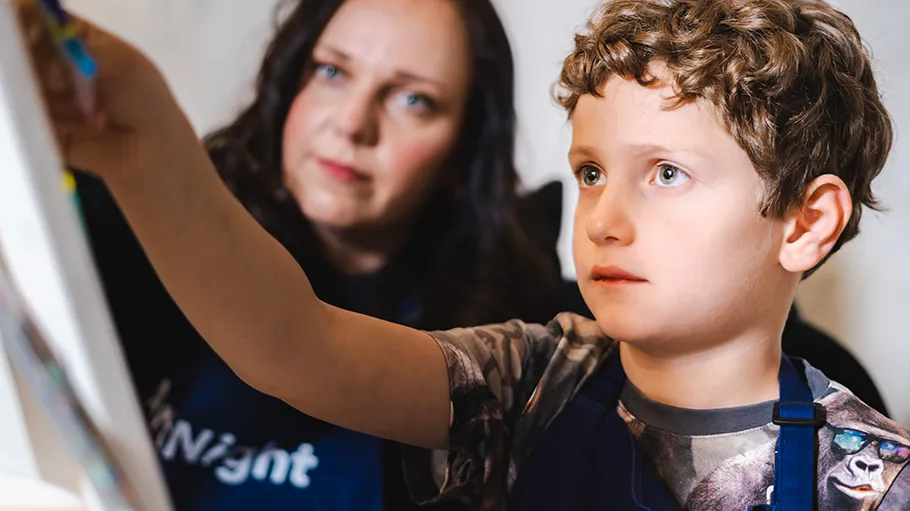 Boy painting with guidance from a woman.