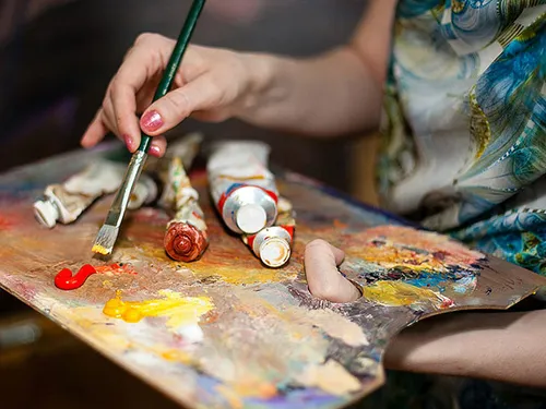 Brush mixes colors on an artist's palette in a studio.