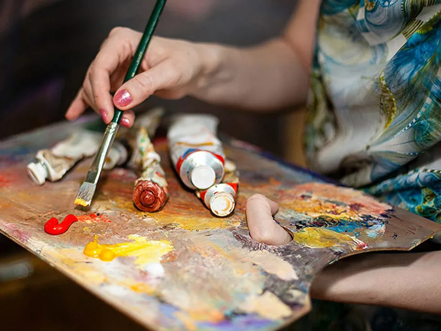 Brush mixes colors on an artist's palette in a studio.