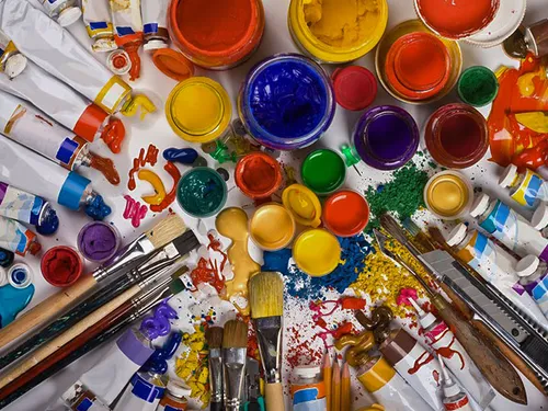 Paints, brushes and accessories lie chaotically on a table.