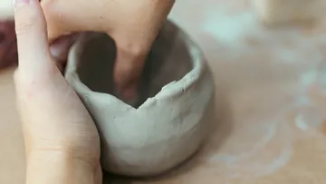Hands shaping clay pot on table.