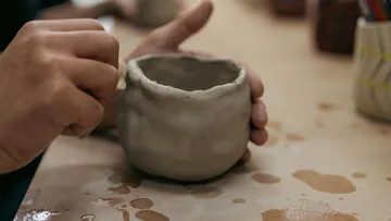 Hände formen Tontopf auf Tisch.