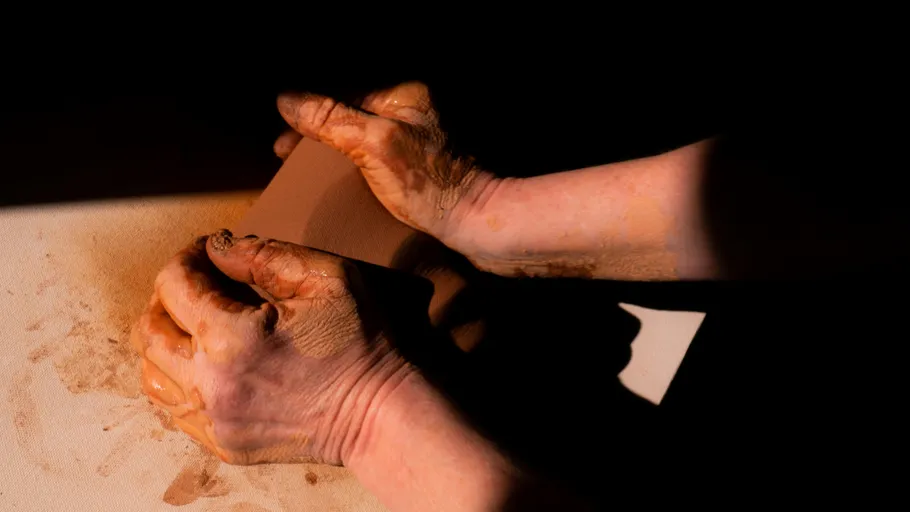 Hands shaping clay on a dark background.