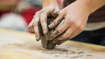 Hands shaping clay on wooden surface.