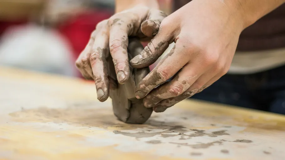 Hands shaping clay on a wooden table.