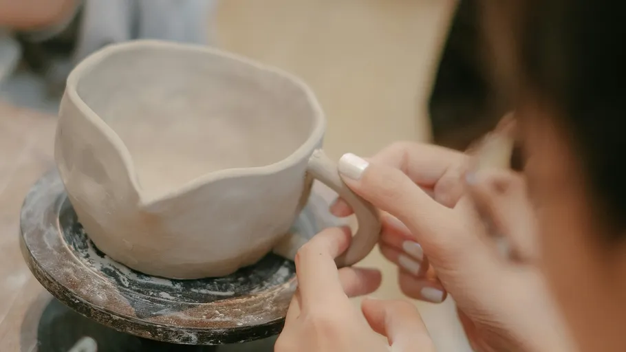 Hands shaping clay mug on pottery wheel.