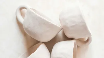 Four white ceramic cups on a neutral background.