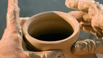 Hands shaping a clay pot on wheel.