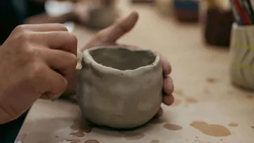 Hands shaping clay cup on table.