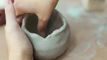Hands shaping clay on a tabletop.