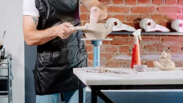 Person sculpting clay on table indoors.