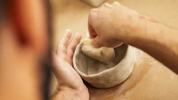 Person shaping a clay pot with sponge.