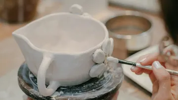 Person painting clay bowl with brush indoors.