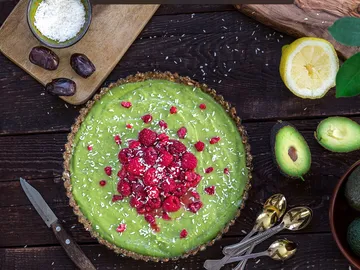 Grüner Kuchen mit Himbeeren und Kokosnuss auf Holzuntergrund.