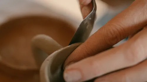 Hands shaping clay with a pottery tool.