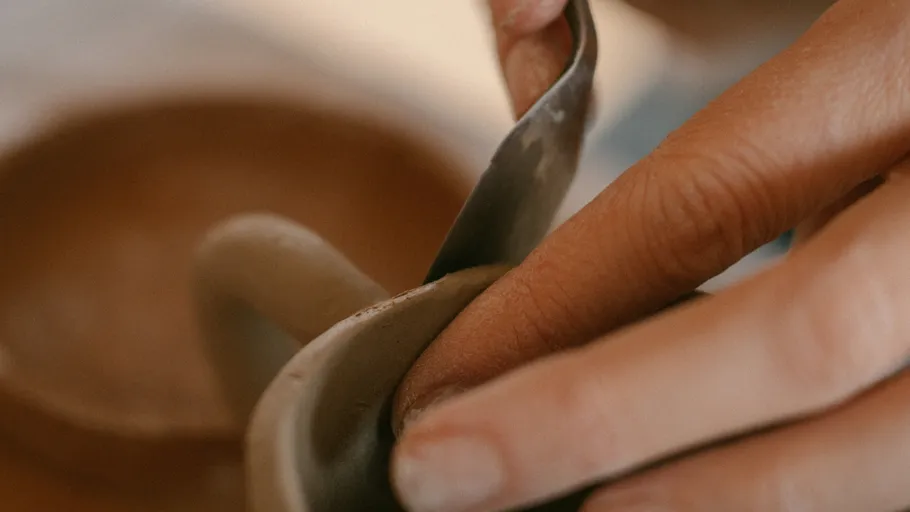 Hands shaping clay with a pottery tool.