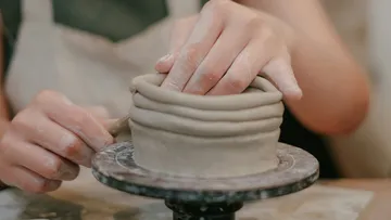Hands shaping clay pottery on a wheel.