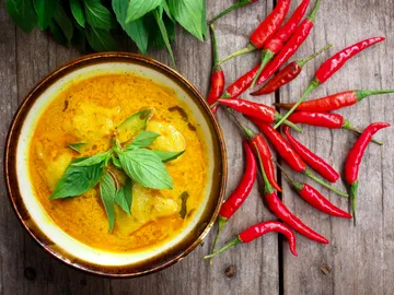 Eine Schüssel mit gelbem Curry und frischen Kräutern, umgeben von roten Chilischoten.