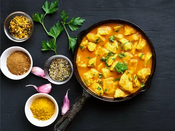 Pfanne mit Hähnchen in würziger Sauce auf Tisch.