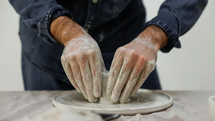 Hands shaping clay on pottery wheel indoors.