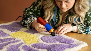 Frau benutzt Tufting-Pistole auf lila Teppich.