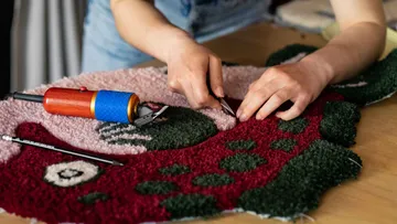 Hands working on colorful textile with tools.