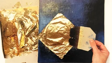 Hand trägt Blattgold auf dunkle Leinwand auf.