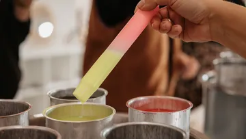Hand taucht einen Stab in bunte Wachstöpfe.
