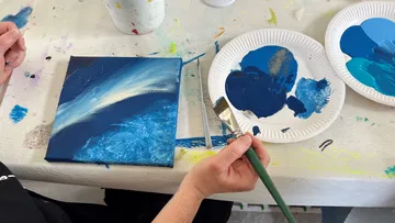 Person painting on canvas with blues on table.