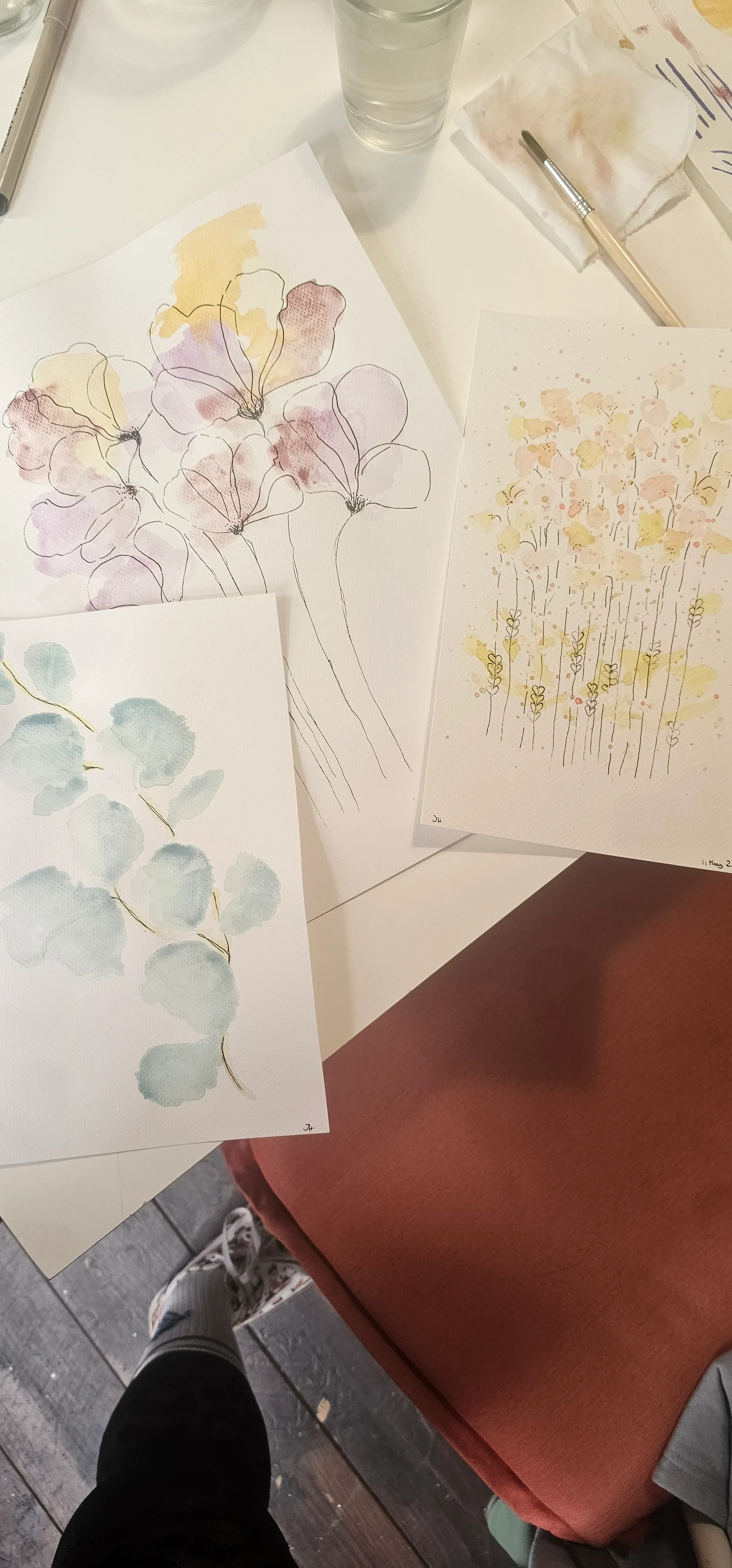 Three watercolor flower paintings on a table.