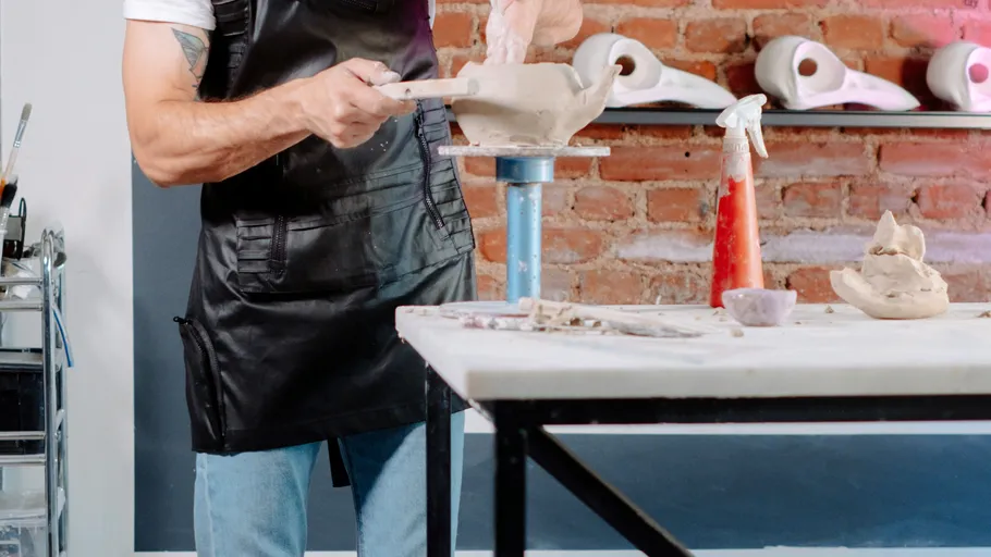 Person shaping clay on a pottery wheel indoors.