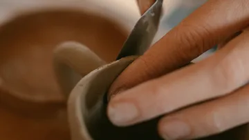 Hände formen Tontasse mit Werkzeug.