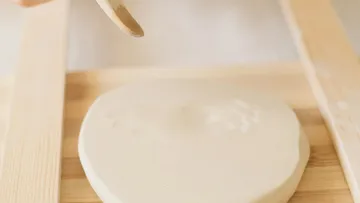 Unbaked dough on wooden board, hand above.