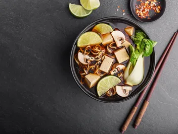 Schwarze Schale mit Nudelsuppe, Tofu und Limette.