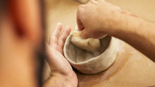 Person smoothing clay bowl with sponge.