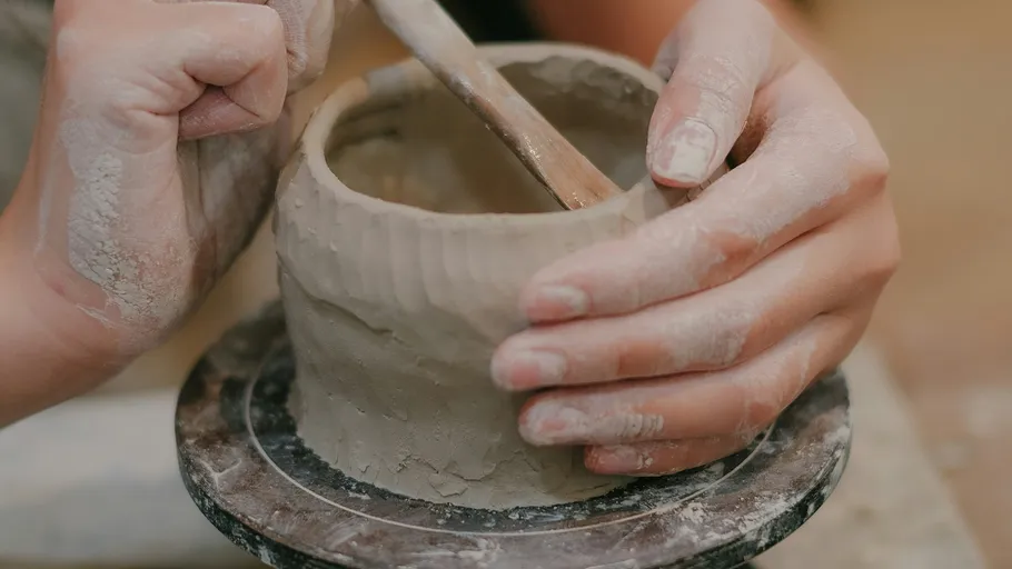 Hands shaping clay pot on pottery wheel.