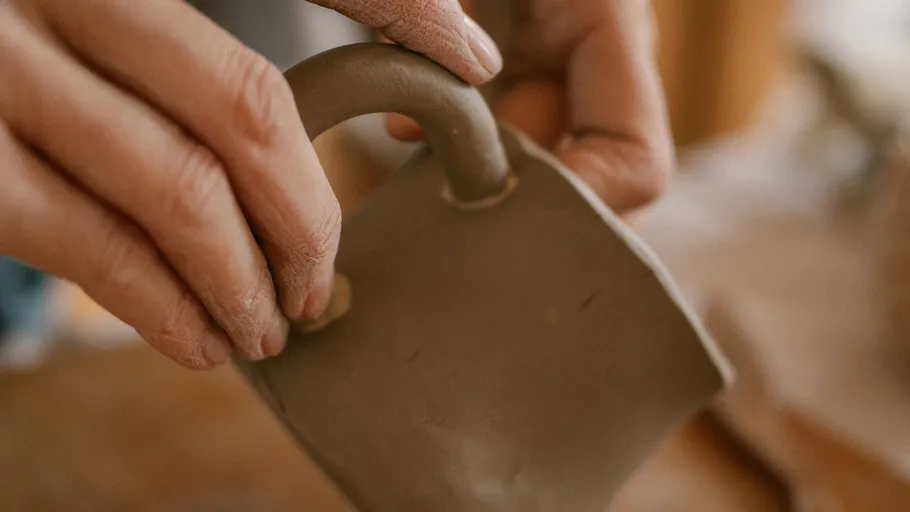 Hands shaping clay mug handle indoors.