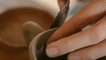 Hands shaping clay with a tool.
